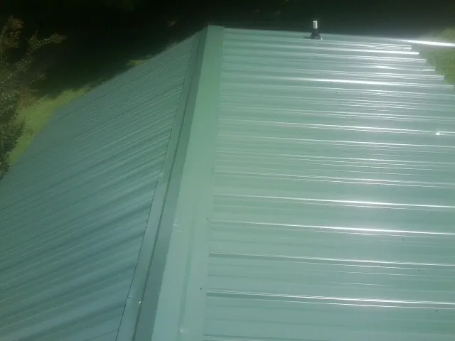 New green metal panels meeting at the ridge of a roof — Flat Roof Repair work by our crew in Bridgeville