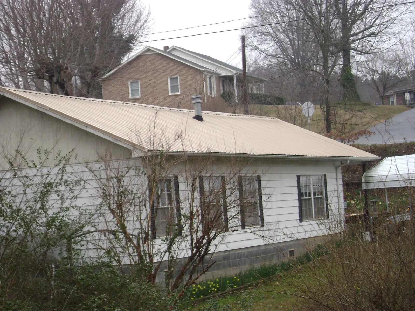 Tan metal roof on a white sided house set into a hillside — Commercial Roofing by Roofing Brothers in Bridgeville