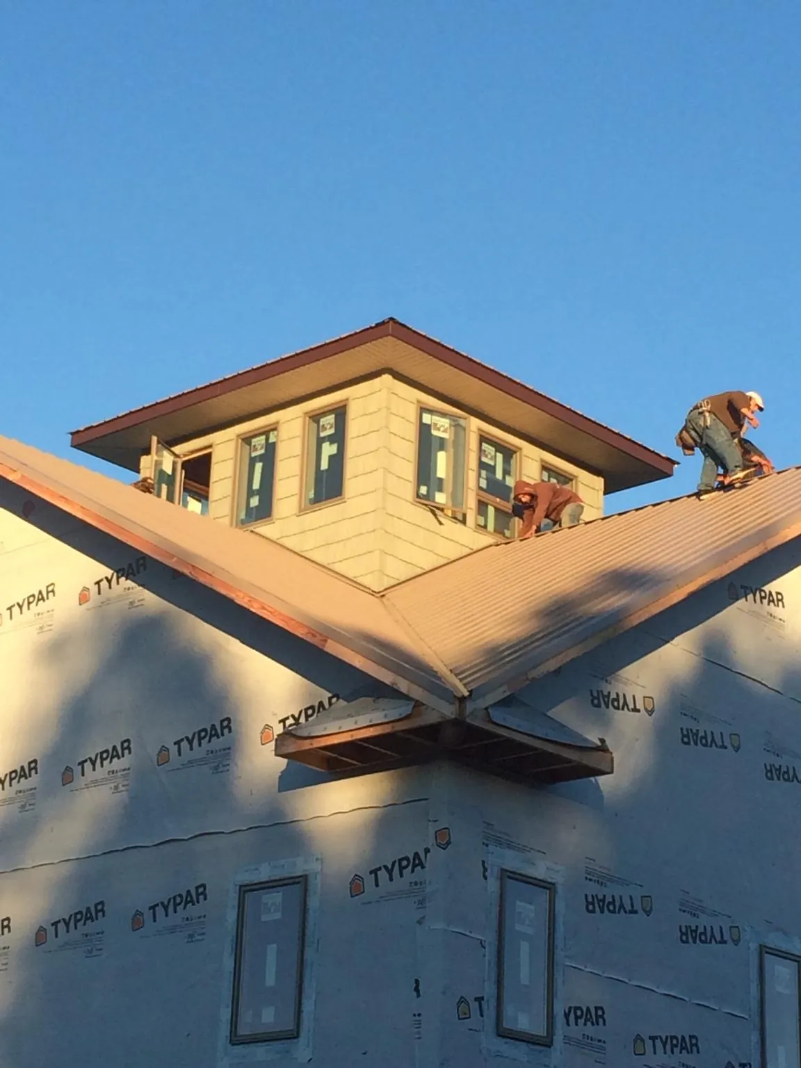 Roofers working around a rooftop cupola on a new metal roof at sunset in Bridgeville